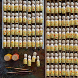 Ein Blick von oben auf eine Ablage mit mindestens 50 handbemalte Nins - Holzfiguren aus dem Sommer-Spiel-Set. Davor liegen Pinsel und 2 kleine Farbtöpfe