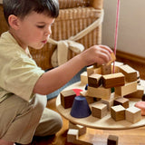 Ein Bub spielt mit "The Pendulum" von Grapat und stapelt verschiedene Holzbausteine auf die Platte.