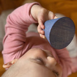 Ein Baby schaut sich einen kegelförmigen Holzbaustein von Grapat Serentipity ganz genau an.