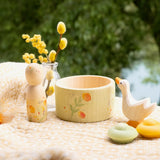 Das kleine Spieleset von Grapat und Ostheimer steht dekoriert auf einem Leinentuch. Man sieht die Nin-figur, das handbemalte Schälchen, die weiße Ostheimer Gas und eine kleine Vase mit Blüten.