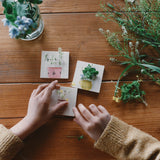 Drei kleine Holzplättchen mit aufgemalten Vasen. Ein Kind verteilt Blüten darauf, sodass es so aussieht, als stecken Blumen in den Vasen.