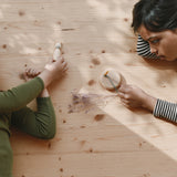 Ein Kind spielt mit einem kleinen Holzkreisel, das andere mit einer Spielfigur aus Holz, beides aus dem Grapat Adventkalender 2025.