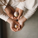 Zwei kleine Holzkugeln, bemalt wie Vögelchen aus einem der Boxen vom Grapat Adventkalender 2025 von Kinderhänden gehalten.