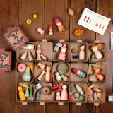 15 kleine Kartonboxen stehen geöffnet auf einer dunklen Holzplatte. Man sieht von oben in die Boxen, die mit kleinen, handbemalten Figuren von Grapat gefüllt sind.