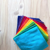 Baumwolltücher von Bauspiel in 12 bunten Farben, gefaltet und im Kreis gefächert nebeneinander, farblich sortiert nach dem Regenbogen liegen.