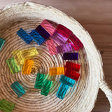 Alle 24 Stück der bunten Lichtbauquader Bausteine von Bauspiel aus Acryl liegen verstreut in einem Korb aus Naturmaterial.