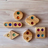 Zwölf "Funkeldächer" Holzbausteine mit bunten Funkelsteinen aus Acryl von Bauspiel in verschiedenen Formen sind auf dem Boden aufgelegt.