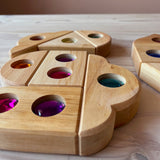 "Funkeldächer" Holzbausteine mit bunten Funkelsteinen aus Acryl von Bauspiel in verschiedenen Formen sind auf dem Boden zu einem Muster gelegt.