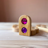 Ein aufgestellter "Funkeldächer" Holzbaustein mit einem Rundbogen und zwei Funkelsteinen aus Acryl in den Farben pink und violett.