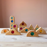 Zwölf "Funkeldächer" Holzbausteine mit bunten Funkelsteinen aus Acryl von Bauspiel in verschiedenen Formen sind auf dem Boden aufgestellt.