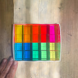 20 transparente, leuchtend bunte Acryl-Bauwürfel von Bauspiel liegen 4x5 Stück nebeneinander in einem flachen, weißen Karton.