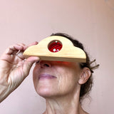 Eine Frau schaut durch den roten Acryl-Funkelstein, der in einem geschwungenen Holzbaustein von Bauspiel eingearbeitet ist.