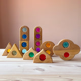 Zwölf "Märchenfenster" Holzbausteine mit bunten Funkelsteinen aus Acryl von Bauspiel in verschiedenen Formen sind auf dem Boden aufgestellt.