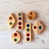 Alle zwölf Märchenfenster Holzbausteine mit bunten Funkelsteinen aus Acryl von Bauspiel in verschiedenen Formen sind auf dem Boden aufgelegt.