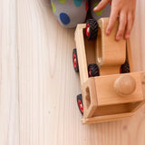 Eine Kinderhand hält der erste Holzauto von Fagus, das auf der Ladefläche des Fagus Unimog geladen ist.