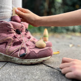 Zwei Holzspielfiguren "Familie Ooh La La" von Grapat stehen auf den Stiefeln eines Kindes. Ein anderes Kind steckt die dritte Figur in den Stiefelschaft.