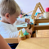 Ein Kind steckt sehr konzentriert kleine, bemalte Holzteile aus dem Set Fancy Nins von Grapat in Löcher eines Holzregals.