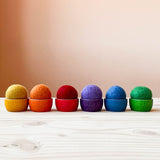 Filzbälle von Kokomoo in sechs verschiedenen Regenbogenfarben in den farblich passenden kleinen Holzschalen liegend.