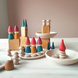 Eine Spielsituation mit bunten, rot-grün-gelben Holzzwergen von Grapat. Sie stehen auf und in Holzschalen und Holztellern. Einige Bausteine stehen in der Landschaft. Auf ihnen stehen kleine grüne Kegel und Minipilze aus Holz.