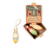 Christbaumschmuck Grapat Winter Sparkles in der Verpackung, ein Anhänger in gelb, blau ist ausgepackt, die Glühkerzen Form und die Bemalung sind schön zu sehen.