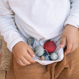 Ein Kind hält den Saum seines TShirts hoch. Darin liegen 5 blau-rote handbemalte Holzkugeln mit Schlinge