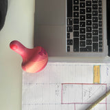 Blick von oben: der Grapat Chill Pink Bird Holzkreisel liegt zwischen einem Laptop und einem Notizbuch.