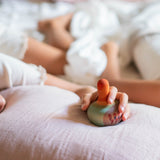 Eine Kinderhand hält den Holzkreisel Mellow Orange Bird von Grapat, der auf einem weichen Kissen steht.