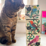 Drei Verpackungsboxen vom Grapat Kreisel aus Holz sind übereinander gestapelt, eine getigerte Katze sitzt daneben und schnuppert ganz vorsichtig daran.