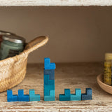 Die eckigen, Tetris-artigen Grapat Mis, Match and Bloom Holzsteine in verschiedenen Blautönen sind teilweise übereinander, teilweise nebeneinander aufgebaut. Links steht ein Korb, rechts eine Holzschale.