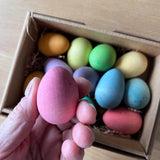 Grapat "Happy Eggs" bunte Eier aus Holz in 12 verschiedenen frühlingshaften Farben liegen in ihrer Kartonverpackung, darüber wird, ganz nah vor der Kamera, ein pinkes Ei gehalten.