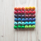 36 Stück Holzperlen von Grimms in Regenbogenfarben farblich sortiert zu einem 6x6 Quadrat aufgelegt.