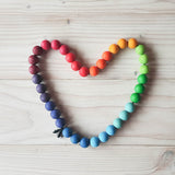 Eine Holzperlenschnur mit Grimms bunten Holzkugeln, aufgelegt in einer Herzform.