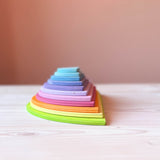 Die 11 halbkreisförmigen Bauplatten von Grimms in pastelligen Regenbogenfarben liegen übereinander gestapelt, wir sehen auf die runden Kanten.