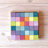 Die 36 Holzbausteine in Würfel Form von Grimms Regenbogen Pastell Mosaik liegen im quadratischen Holzrahmen.