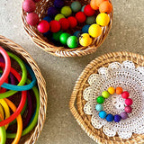 Drei Körbe von oben, in einem liegt ein Grimms Perlengreifling in Regenbogenfarben, in einem anderen Motorikringe und im dritten Perlen aufgefädelt auf einer Schnur.