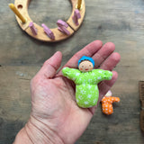 Das kleine Grimms Waldorf Püppchen Baby Leo in grün mit blauer Haube liegt in einer Handfläche.