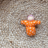 Das kleine Grimms Püppchen Baby Mia in orange mit rosa Haube.