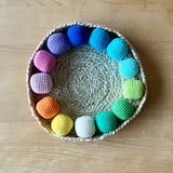 Häkelbälle von Kokomoo im Kreis in einem Korb aufgelegt, in dreizehn unterschiedlichen Farben sortiert.