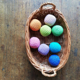 In einem kleinen Korb mit Tragegriffen liegen acht Häkelbälle von Kokomoo in verschiedenen Farben.