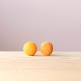 Ein gelber Häkelball von Kokomoo und eine gelbe Filzkugel in der gleichen Größe liegen nebeneinander.