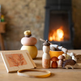 Das Spiele- und Forscherset für Kinder "Hello Autumn" von Grapat und Ostheimer steht auf einem Tisch vor dem Kamin. Der Igel, die beiden Holzpilze, die Nins Spielfigur und die kleine Blätterpresse.