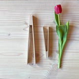 Die Holzzange von Kokomoo und die Holzzange Mini von Grapat liegen neben einer Tulpe zum Größenvergleich, die eine fast so groß wie die Tulpe, die Mini-Greifzange aus Holz halb so groß.
