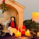 Ein Blick in eine Weihnachtskrippe für Kinder, mit Maria, zwei kleinen Filzschafen, einem kleinem roten Holzzwerg asl Hirte, davor Teelichter und eine Strohstern.
