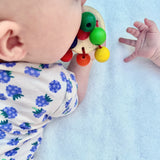 Ein Baby erkundet mit dem Mund die Regenbogenrassel aus speichelecht lackiertem Holz von Nic Toys.