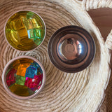 Lichtbauwürfel von Bauspiel in verschiedenen Farben liegen in kleinen Schüsseln aus Edelstahl, die in einem Korb aus Naturmaterial stehen.