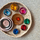 7 Lichtbauwürfel von Bauspiel in verschiedenen Farben liegen in kleinen Klangschalen als Edelstahl oder einem Holzteller, die wiederum in einem Korb aus Naturmaterial stehen.