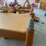 Eine kleine Holzfigur in Blau steht auf einem zylinderförmigen Tischbein in einem Spielraum.