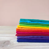 Ein Stapel bunter Baumwolltücher von Kokomoo in 12 bunten Farben, gefaltet aufeinander liegend, sortiert nach dem Regenbogen.