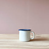 Ein weißer Tasse aus Emaille mit blauem Rand von Kokomoo.