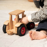 Der Fagus Schlepper Spieltraktor aus Holz, ein Baby sitzt daneben und spielt damit.
